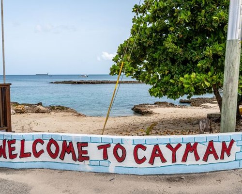 Welcome to Cayman sign with a beach and leafy trees behind it