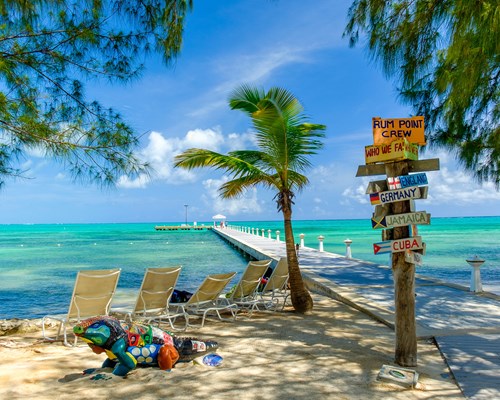 A colourful sign next to deckchairs laid out on a beach with a view of the bright blue sea - Rum Point Beach