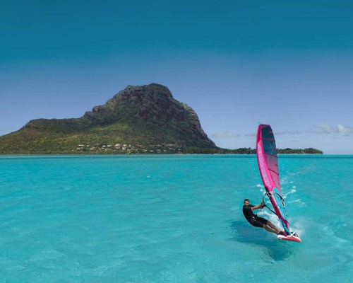 Man parasailing in the middle of turquoise sea with mountains in the background