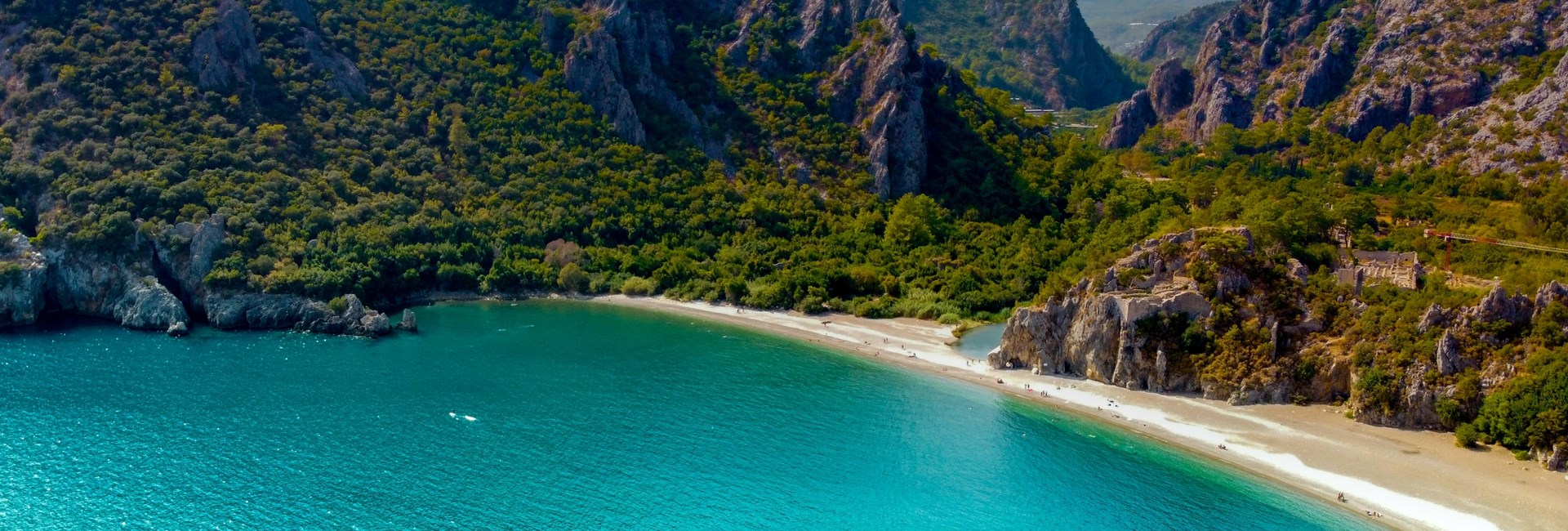 Sarsala Koyu Cove with turquoise sea in foreground, yellow sandy beach and verdant mountain backdrop