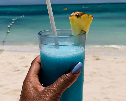 Woman with blue painted nails holding a blue cocktail in a tall glass at Jamaican beac