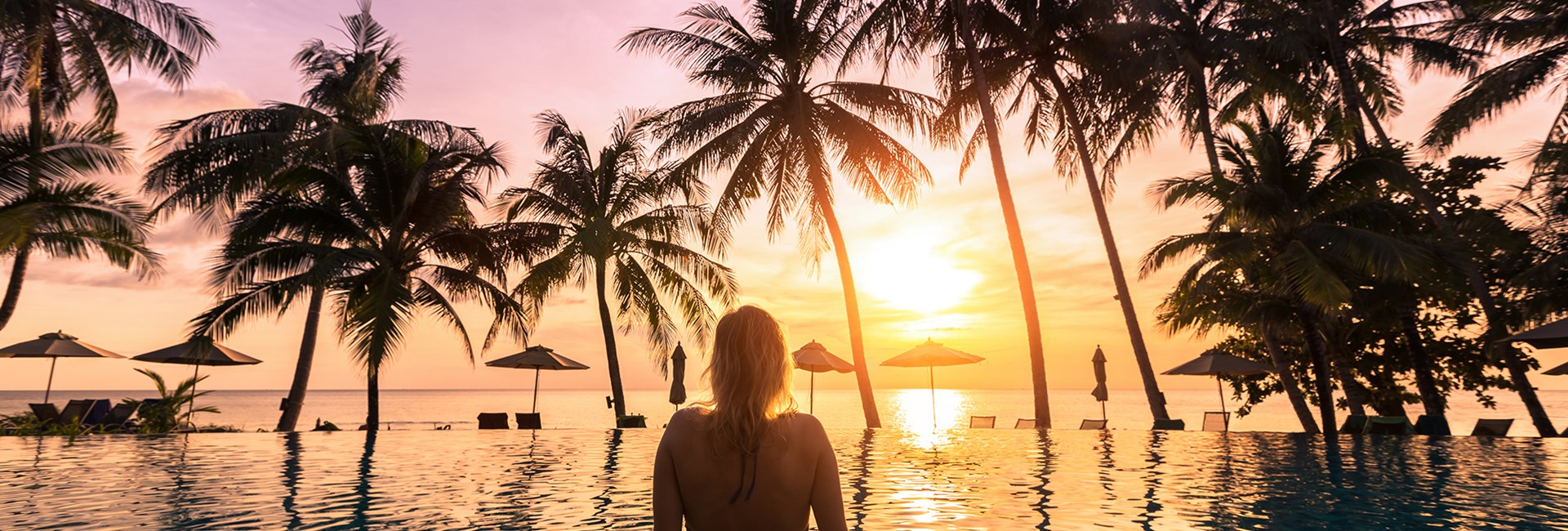 woman relaxing by infinity pool of luxury hotel watching sun set into sea