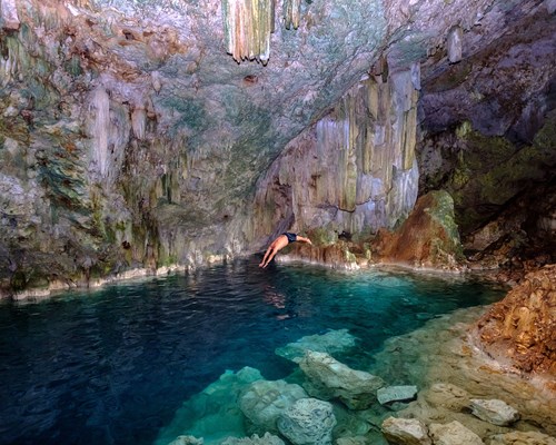 Man diving into a crystal clear freshwater pool in an underground cave