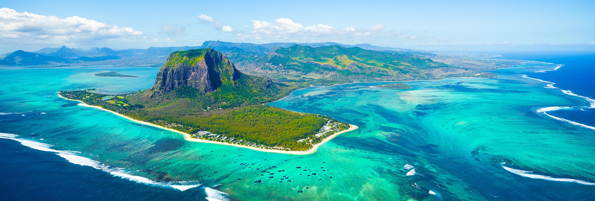Aerial view of mountainous tropical island surrounded by shallow reefs and clear turquoise sea