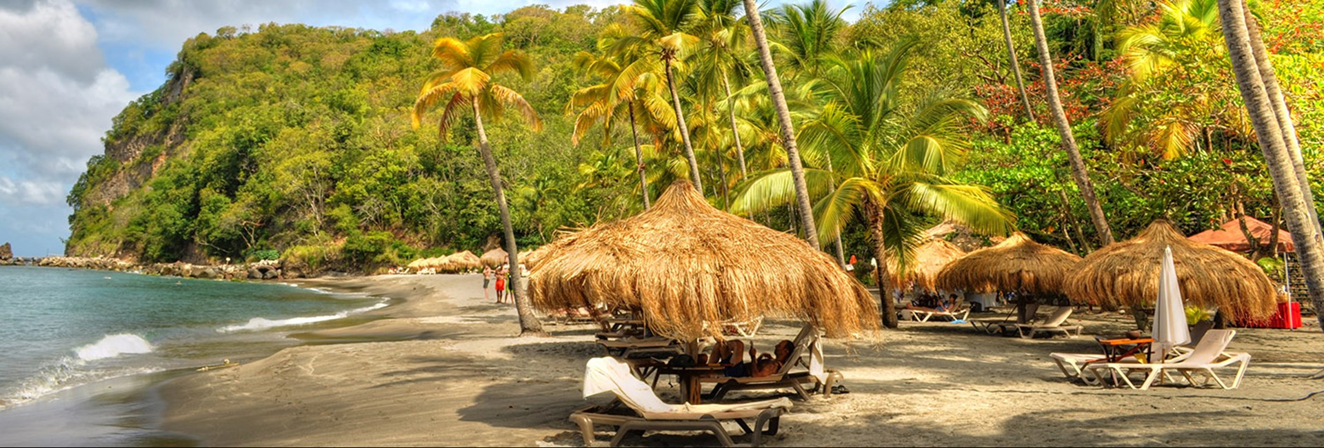Caribbean beach with dark sand and straw umbrellas and sun loungers for guests