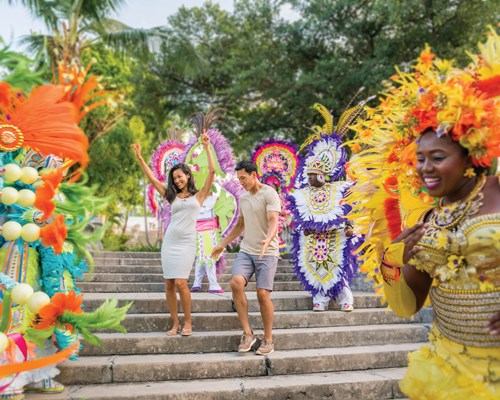Couple standing among carnival dancers dressed in colourful costumes