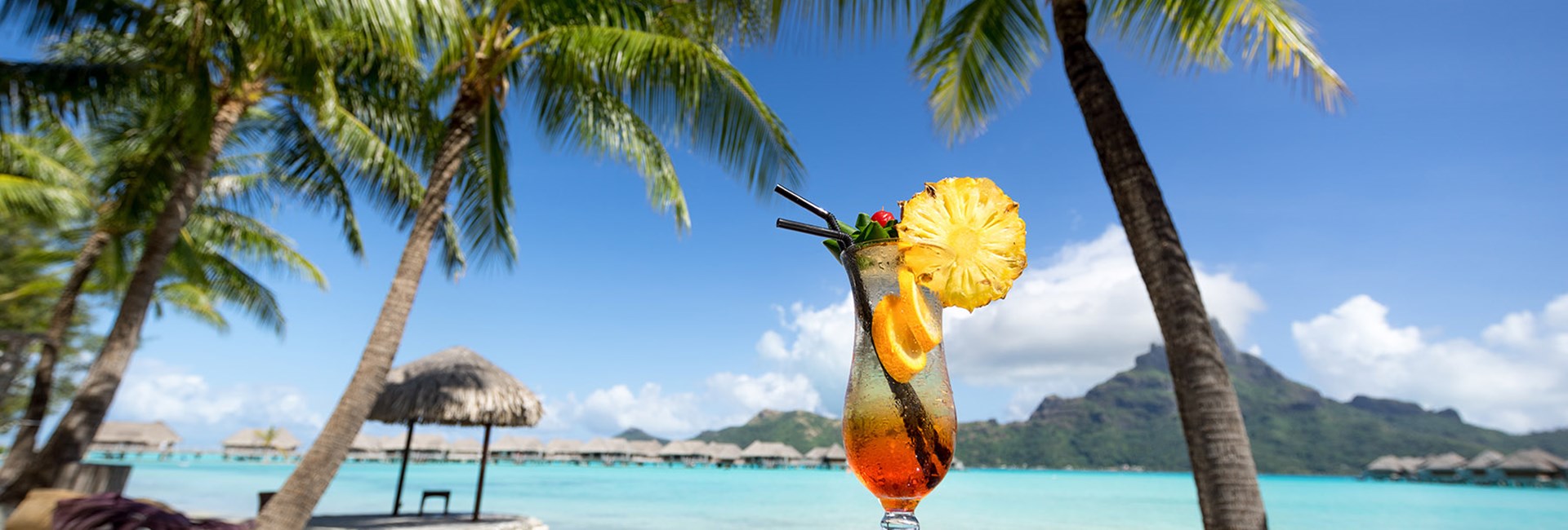 orange cocktail on edge of pool next to beach with palm trees