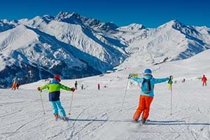 Family skiing down a piste with their arms in the air