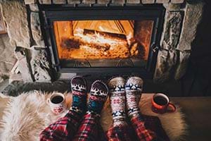 2 sets if feet, wearing knitted socks, sitting next to a log fire